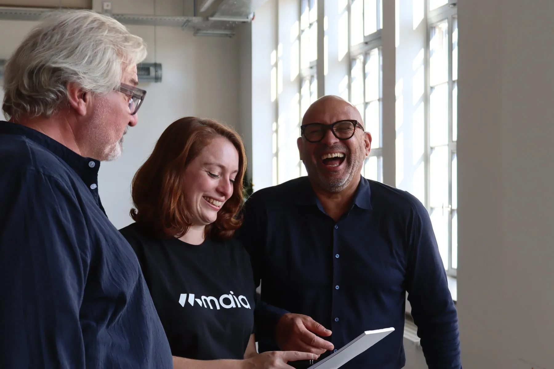 Three colleagues laughing together over a tablet