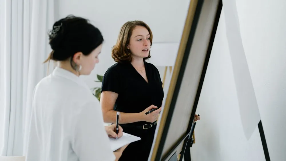 Carolin erklärt am Flipchart, eine Kollegin schreibt mit