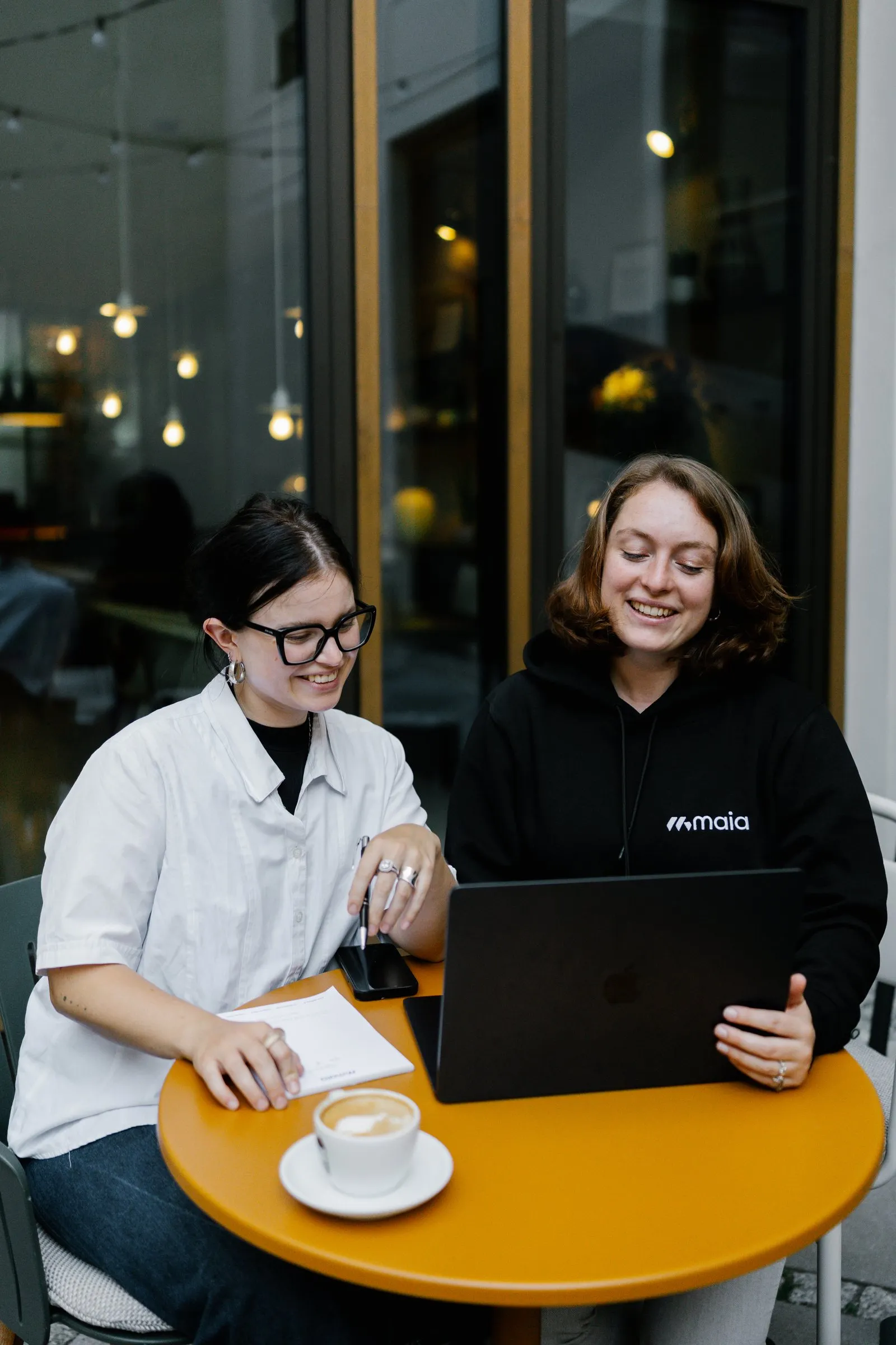 Zwei Kolleginnen lachen gemeinsam am Laptop im Café