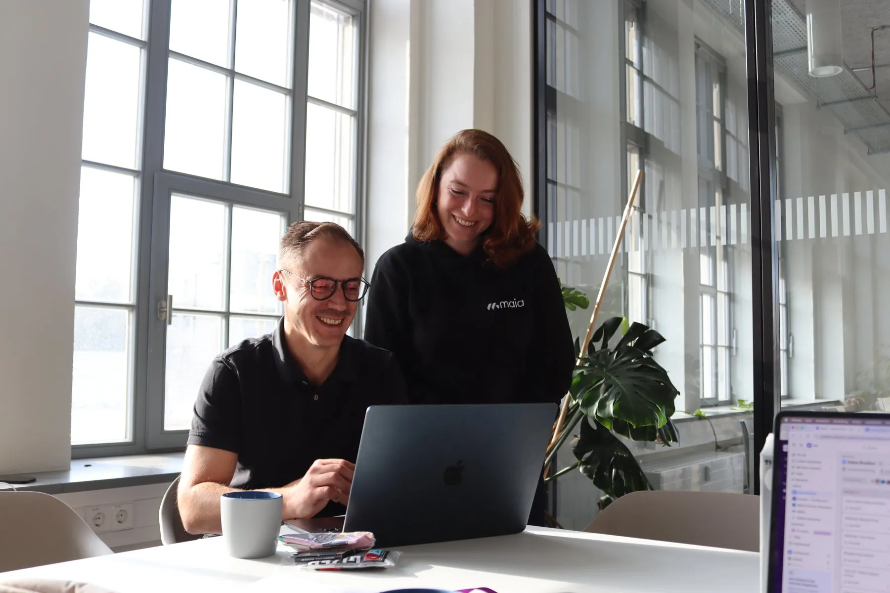 Zwei Kolleg:innen von MAIA lachen gemeinsam am Laptop
